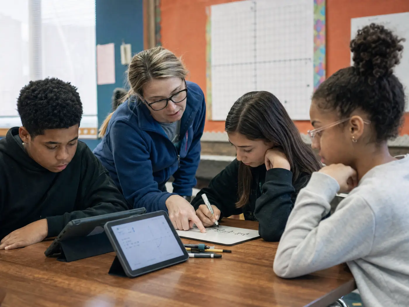 Middle-school students working a math problem on tablets with their teacher beside them